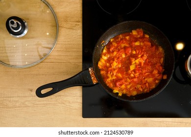 Overhead View Of Frying Pan With Tomato Sauce On Modern Electric Stove, The Glass Lid Lies Next To It