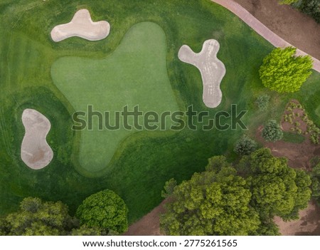 Overhead view of a golf course putting green surrounded by multiple sand bunkers, manicured fairway grass, and lush green trees along the perimeter