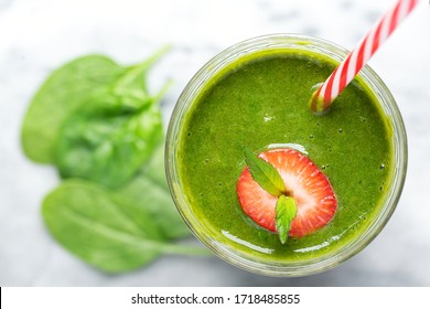 Overhead View Of A Green Spinach Smoothie With Strawberry Garnish And A Red Striped Drinking Straw