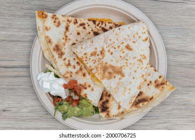 Overhead View Of Grilled Quesadilla Cut Into Quarters Served With A Generous Scoop Of Sour Cream And Guacamole For Lunch.