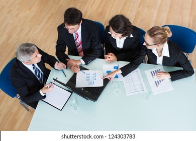 Overhead View Of A Group Of Diverse Business Executives Holding A Meeting Around A Table Discussing Graphs Showing Statistical Analysis