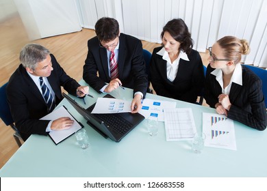 Overhead View Of A Group Of Diverse Business Executives Holding A Meeting Around A Table Discussing Graphs Showing Statistical Analysis