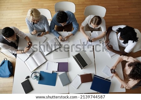 Overhead view group of multi ethnic students use smartphones sit at shared table in classroom. Mobile application usage at break, young gen Z modern wireless tech overuse, bad habit, lifestyle concept