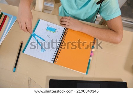 Overhead view of the hand of schoolboy holding compass, drawing circle while solving problems in an online geometry lesson. New knowledge. Back to school. New semester of an academic year. Copy space