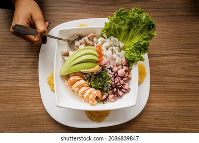 Overhead View Of A Hand Taking Ceviche From A Seafood Platter With Fish, Octopus, Crab, Shrimp, And Avocado. Seafood