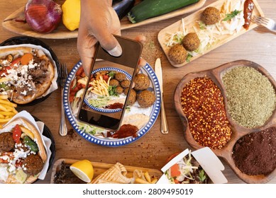 Overhead view of hand using smartphone capturing middle eastern food and spices on a table