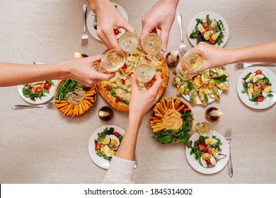 Overhead View Of Hands Clinking Glasses Over A Table With Italian Cuisine Assorti. Margarita, Cheese Sticks With Hummus And Arugula, Salad With Tomatoes And Eggs Served With White Wine.