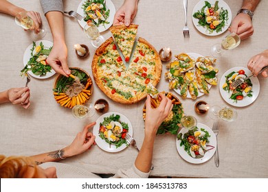 Overhead View Of Hands Of Dining People Over A Table With Italian Cuisine Assorti. They Are Eaing Margarita, Cheese Sticks With Hummus And Arugula, Salad With Tomatoes And Eggs Served With White Wine.