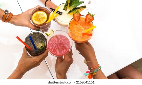 Overhead view of hands toasting multicolored fancy tropical blended cocktails in a social gathering.