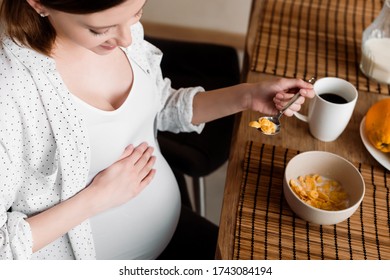 Overhead View Of Happy And Pregnant Woman Holding Spoon With Tasty Corn Flakes Near Cup With Tea