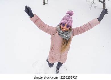 Overhead view of happy woman with raised hands fooling around in the snow outdoor. High quality photo - Shutterstock ID 2256252927