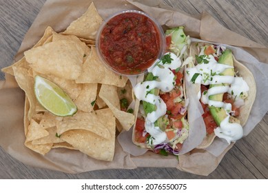 Overhead View Of Hearty Basket Full Of Chips And Salsa To Eat With Three Fish Tacos.