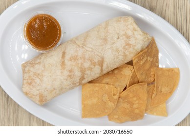 Overhead View Of Hearty Burrito Wrapped In Flour Tortilla And Served With Chips And Salsa On The Side.