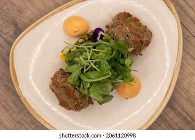 Overhead View Of Hearty Plate Of Roasted And Fried Crab Cakes With A Dallop Of Sauce And Arrranged On A Plate With Arugula.