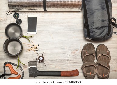 Overhead View Of Hiking Gear Laid Out For A Trip On A Rustic Wood Floor. Gear Include, Compass, Phone, Tent, Ax, Gas, Burner, Matches, Shoes.