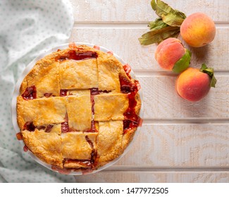 Overhead View Of Homemade Peach Pie On A White Wooden Surface With Raw Peaches