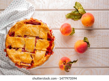 Overhead View Of A Homemade Peach Pie On A White Wooden Surface With Raw Peaches