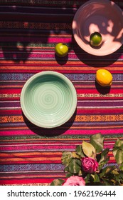 Overhead View Images Of Pink And Pastel Green Soup Plates, Two Lemons, And Lime On A Colorful Table Cloth Shot In The Sunlight