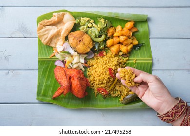 Overhead View Of Indian Woman Eating Biryani Banana Leaf Rice On Wooden Dining Table.