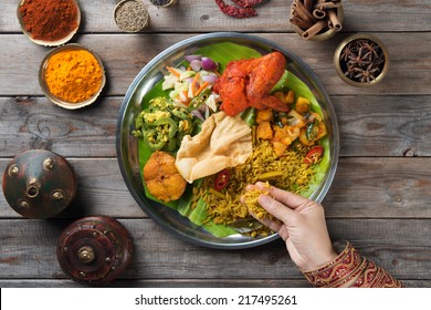 Overhead View Of Indian Woman's Hand Eating Biryani Rice On Wooden Dining Table.