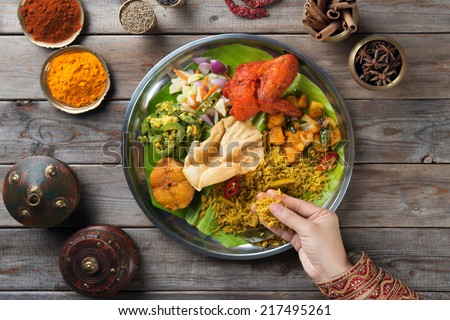 Overhead view of Indian woman's hand eating biryani rice on wooden dining table.