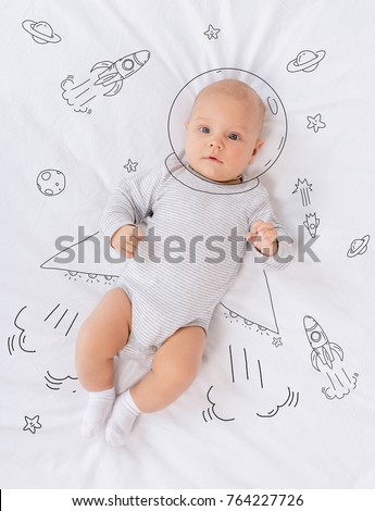 overhead view of innocent caucasian baby astronaut lying on bed