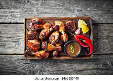 overhead view of Jerk Chicken on a rude board with sauce and lemon on a rustic wooden table, horizontal view from above, close-up, flatlay