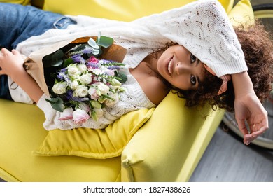 Overhead View Of Joyful And Curly Woman With Flowers Lying On Couch