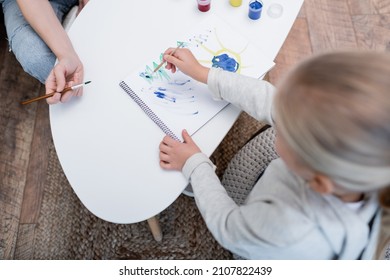 Overhead View Of Kid Drawing On Sketchbook Near Mom With Paintbrush At Home