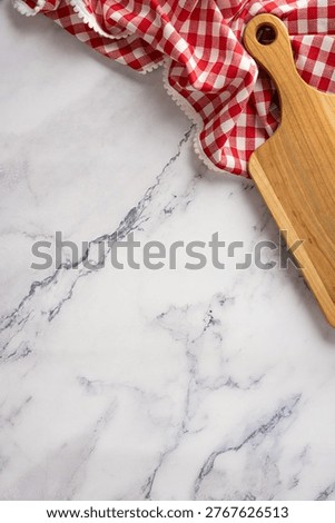 Overhead view of kitchen cooking preparations on a marble countertop featuring a wooden cuttingboard and a red checkered cloth for rustic food styling