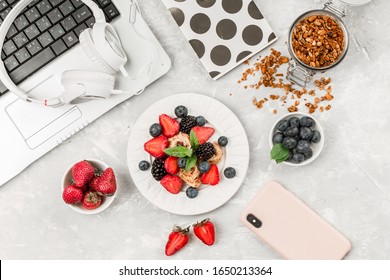 Overhead View Of Laptop, Fresh Breakfast With Fruit, Headphones And Mobile Phone On White Desktop Table.Top View And Flat Lay. Woman Business And Breakfast Concept. 