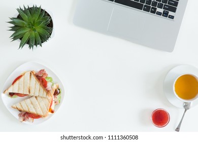 Overhead View Of Laptop, Fresh Sandwich, Cup Of Green Tea And Mobile Phone On White Desktop Table. Woman Business And Breakfast Concept, Top View And Flat Lay