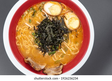 Overhead View Of Large Bowl Of Spicy Volcano Ramen Served With A Pile Of Seaweed On Top With Braised Pork And Hard Boiled Egg Halves.