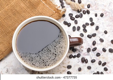 Overhead View Of A Large Coffee Mug On Granite Countertop With Spilled Coffee Beans Horizontal Format