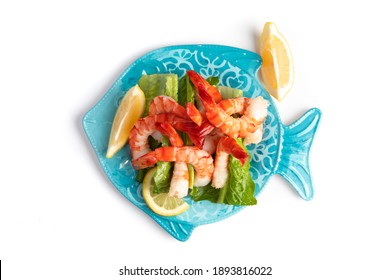 Overhead View Of Large Cooked Peeled Tiger Shrimps On A Blue Fish  Shaped Plate With Lemon Wedges And Tangy Sauce Isolated On White