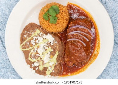 Overhead View Of Large Slap Of Chile Colorado Entree Meat, Refried Beans, And Rice Drenched In The Red Sauce.