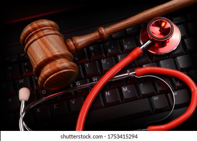 An Overhead View Of A Legal Wood Gavel And Doctors Stethoscope Resting On Top Of A Black Keypad And Some Red Gel Lighting Striking The Scene.