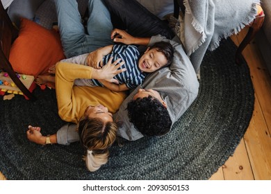 Overhead view of a little boy having fun with his mom and dad in their play area. Young boy laughing cheerfully while lying on top of his parents. Family of three spending some quality time together. - Powered by Shutterstock