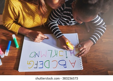Overhead view of little girl learning the alphabet using coloured crayons