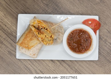 Overhead View Of Loaded Breakfast Burrito With Meat And Eggs Cut In Half For Easier Handling Served With Salsa.