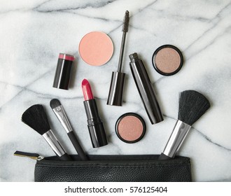 Overhead View Of Make Up Products Spilling Out Of A Black Cosmetics Bag, On A White Marble Counter Top Background