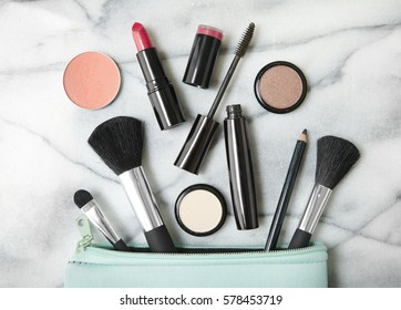 Overhead View Of Make Up Products Spilling Out Of A Pastel Blue Cosmetics Bag, On A White Marble Counter Top Background