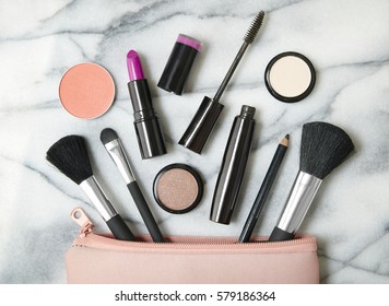 Overhead View Of Make Up Products Spilling Out Of A Pastel Pink Cosmetics Bag, On A White Marble Counter Background