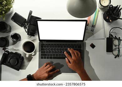 Overhead view of male photographer using laptop on white table with digital camera, memory card and lens - Powered by Shutterstock