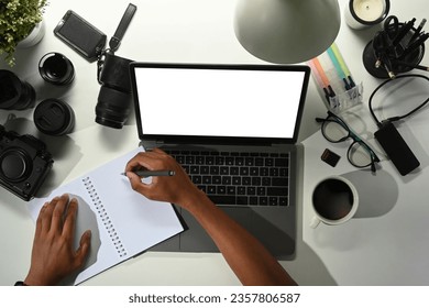 Overhead view of male photographer using laptop on white table with digital camera, memory card and lens - Powered by Shutterstock