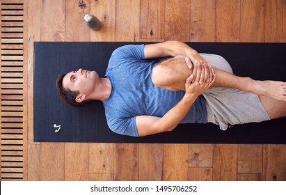 Overhead View Of Man Lying On Exercise Mat On Wooden Floor