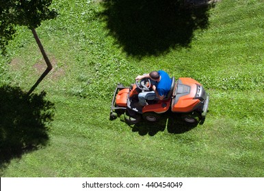 Overhead View Of A Man Mowing The Lawn On An Orange Ride On Mower With The Shadows Of Trees In A Concept Of Yard Maintenance