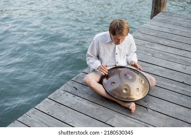 Overhead View Of Man Playing Hang Drum On Wooden Pier Above River In Venice