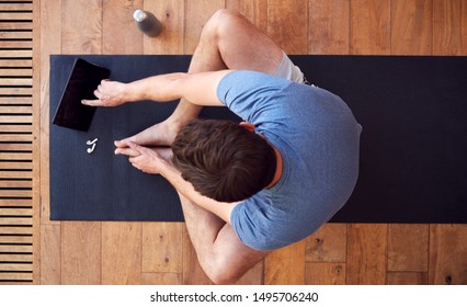 Overhead View Of Man Sitting On Exercise Mat Using Digital Tablet