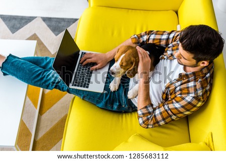 Photo of overhead view of man using laptop on sofa with cute dog